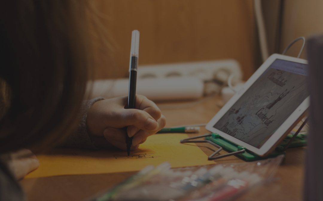 Close up of woman writing with a pen on paper in front of an ipad