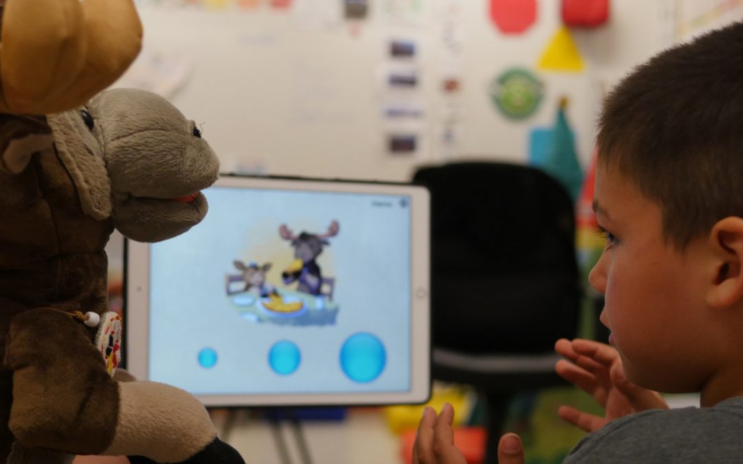 Closeup of Child using Antle Discovers His Voice ipad application beside Antle the Moose Puppet